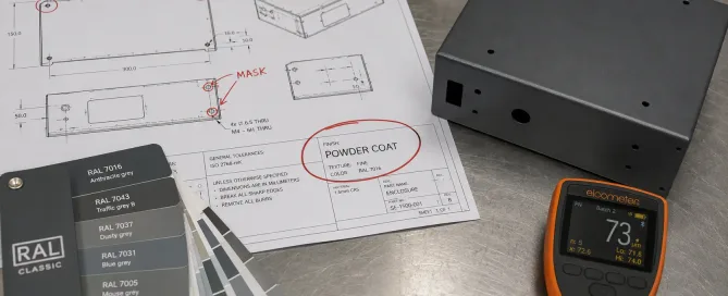 Engineering drawing with powder coating callout annotations next to a coated sheet metal part on a workbench